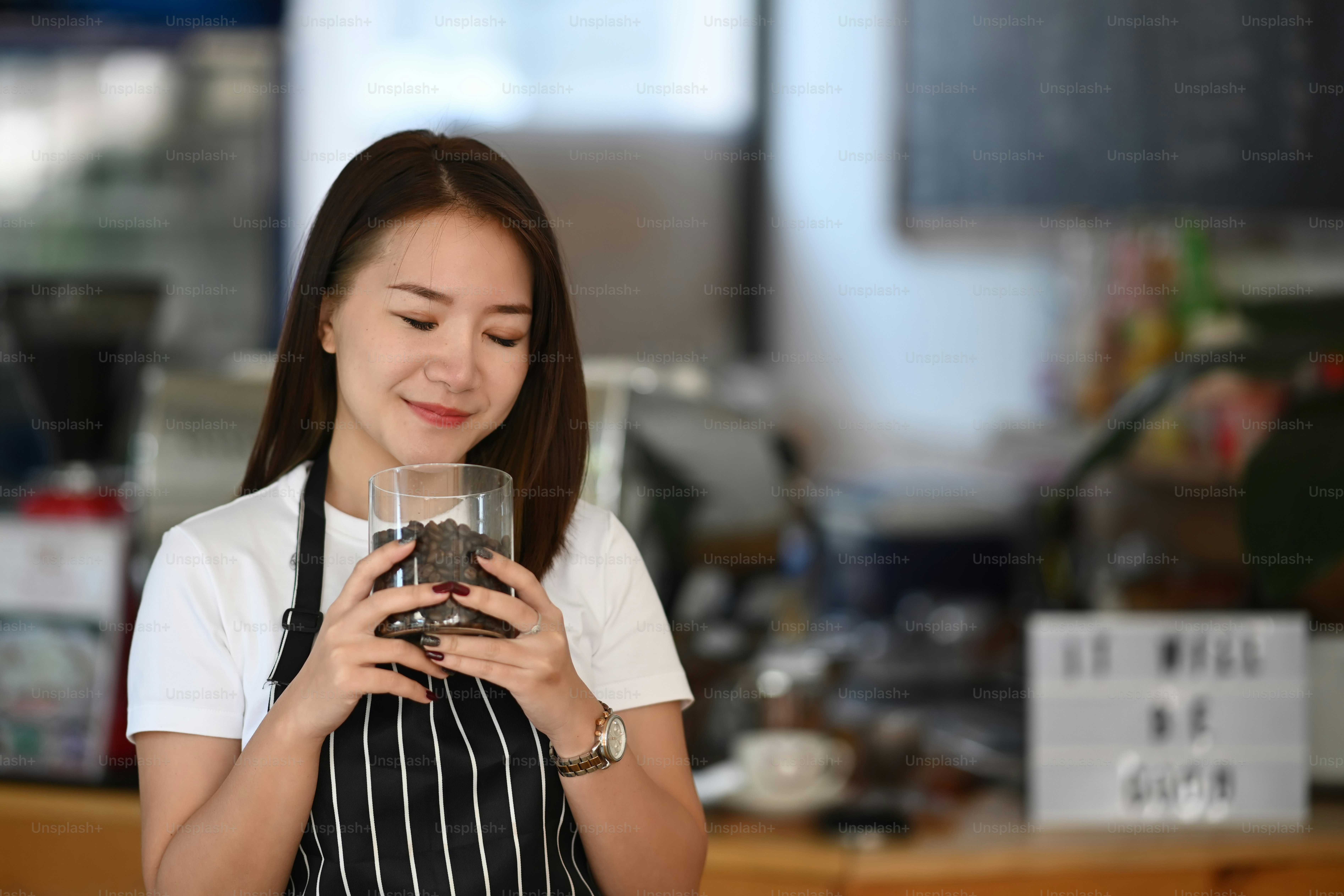Young woman barista smelling and checking quality of coffee beans at coffee shop.