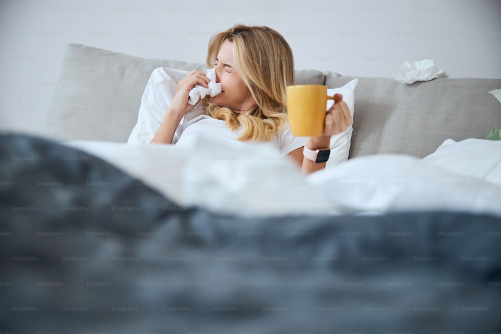 Cute woman sitting under the blanket and holding cup in left hand