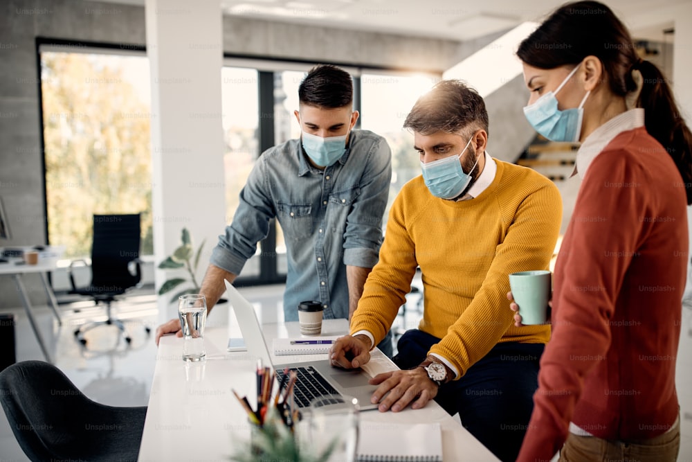 Group of entrepreneurs with face masks cooperating while working on a computer in the office.