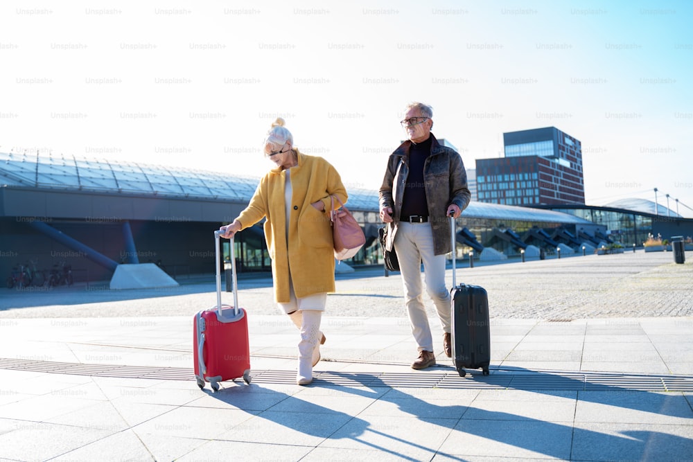Seniors couple walking on the train station. Two mature people wearing protective masks. Tourist after the city break. Travel and relationship concept during a pandemic. Outdoor photo.