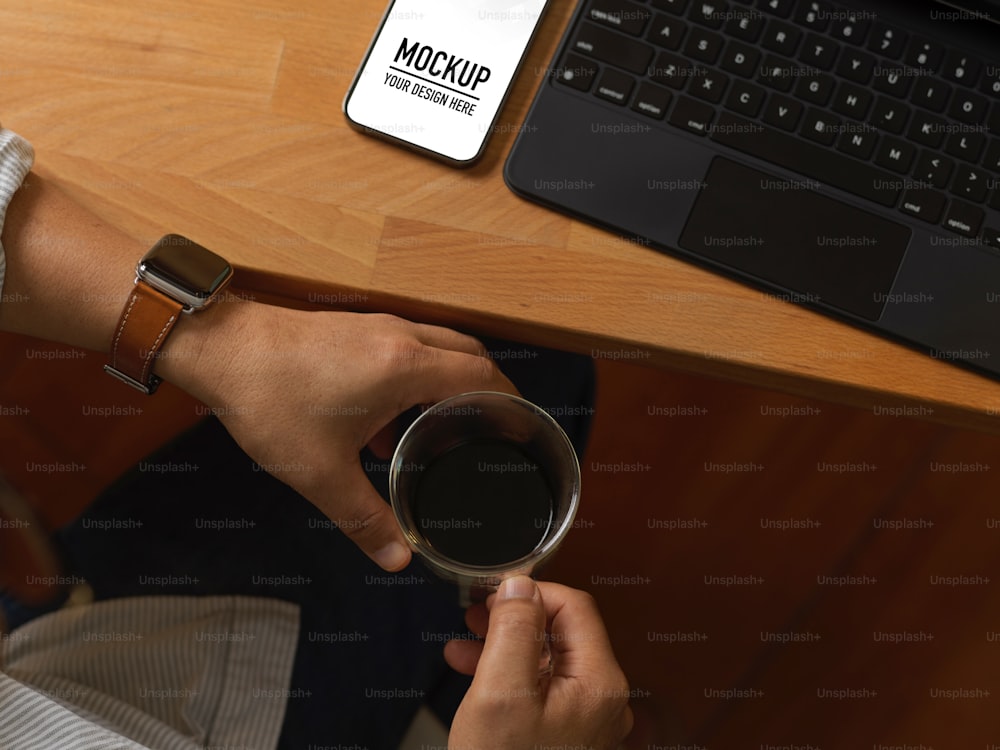 Top view of male hands holding coffee cup while sitting at workspace with smartphone and laptop