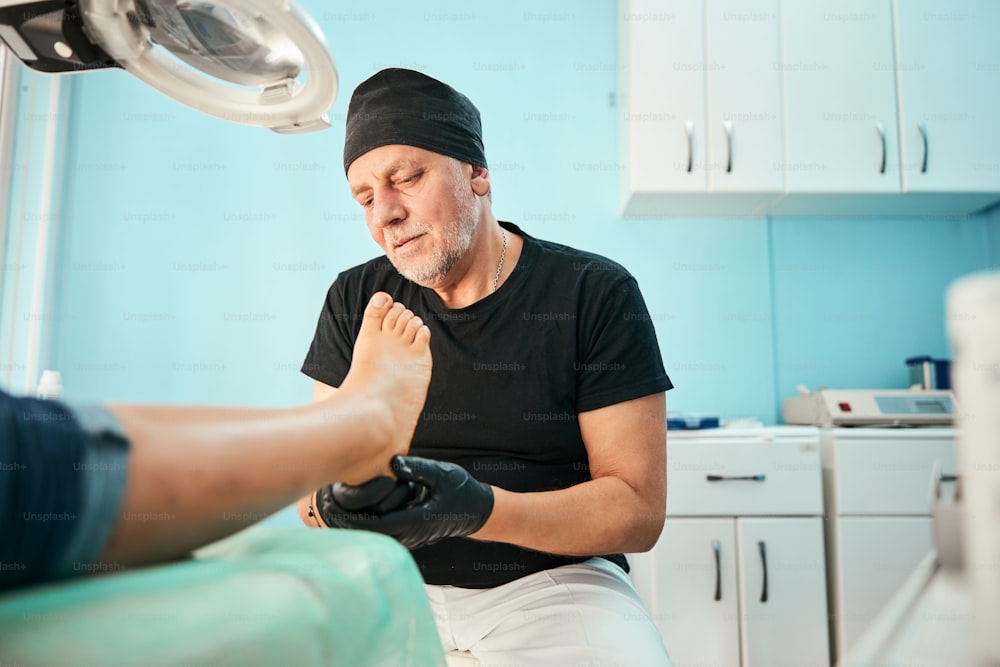 Attentive podologist sitting at his workplace while going treating medical massage