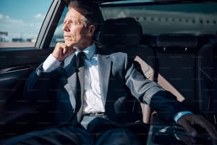 Pensive mature man in elegant suit is sitting on back seat after landing by plane