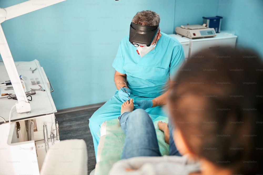 Attentive male person sitting near his patient and using nail clippers instrument