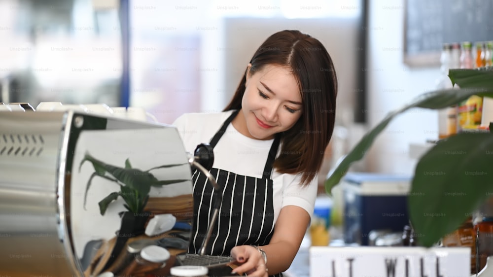 Asian woman owner barista using coffee machine for making coffee in the cafe.