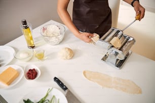 Photo recadrée d’une femme plaçant des morceaux de pâte dans une machine à pâtes tout en cuisinant à la maison