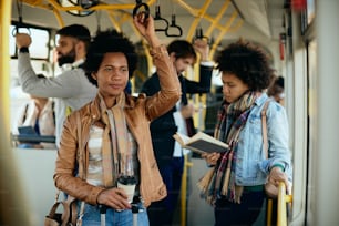 Mujer negra adulta mediana que lleva café para llevar mientras viaja en autobús.
