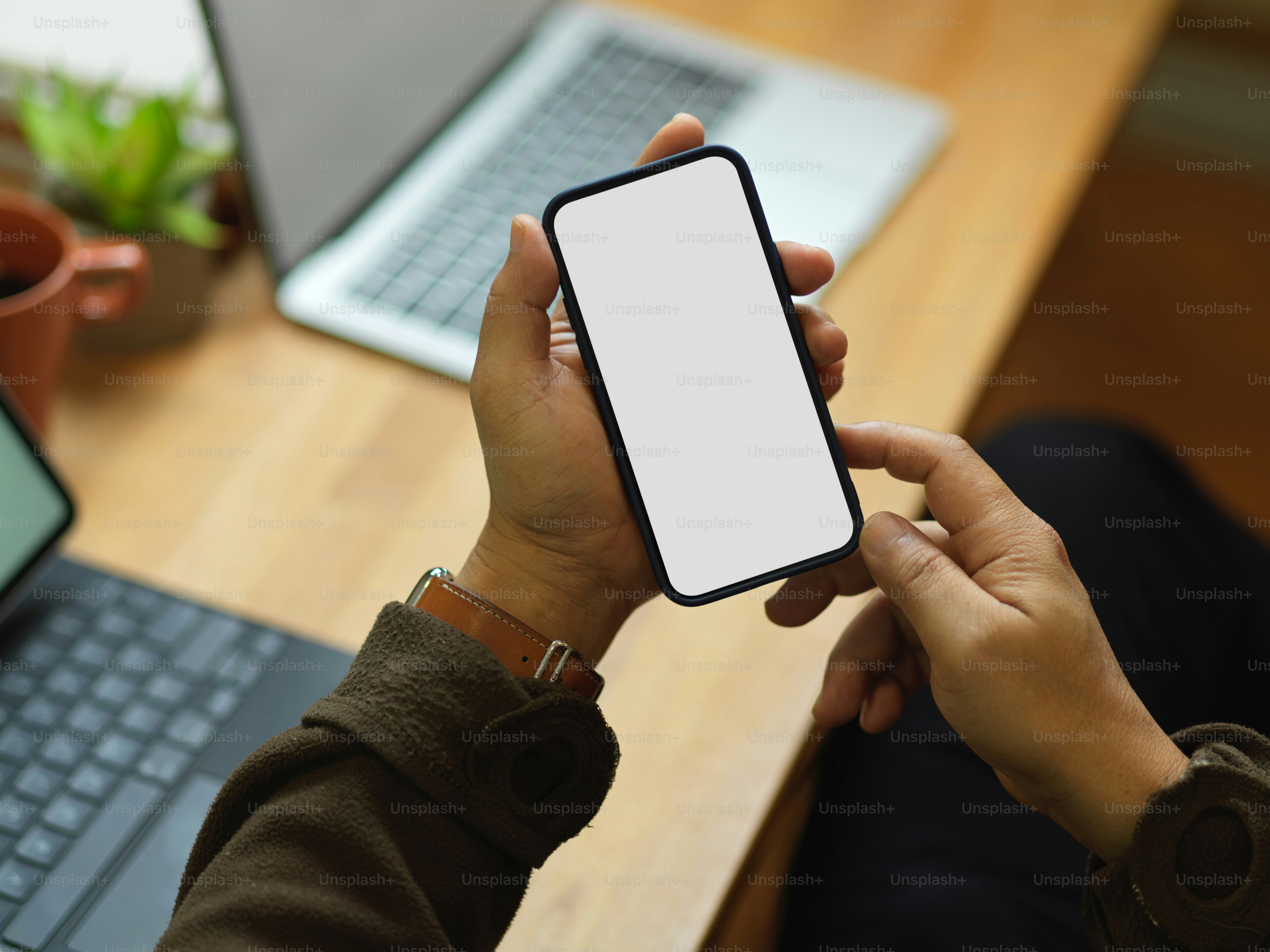 Colpo ritagliato della mano maschile che usa lo smartphone mentre è seduto sul posto di lavoro