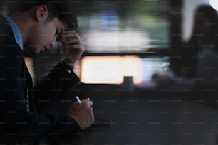 Side view of stressed businessman sitting in office and working on digital tablet.