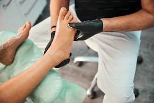 Focused photo on male person wearing black gloves during procedure with cream