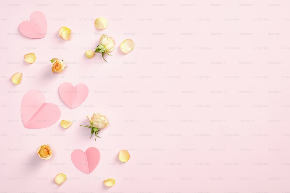 ピンクの背景に紙のハート、バラの花、花びらを持つフラットレイ構図。ロマンチック、愛、バレンタインデーのコンセプト。コピー領域付きの上面図。