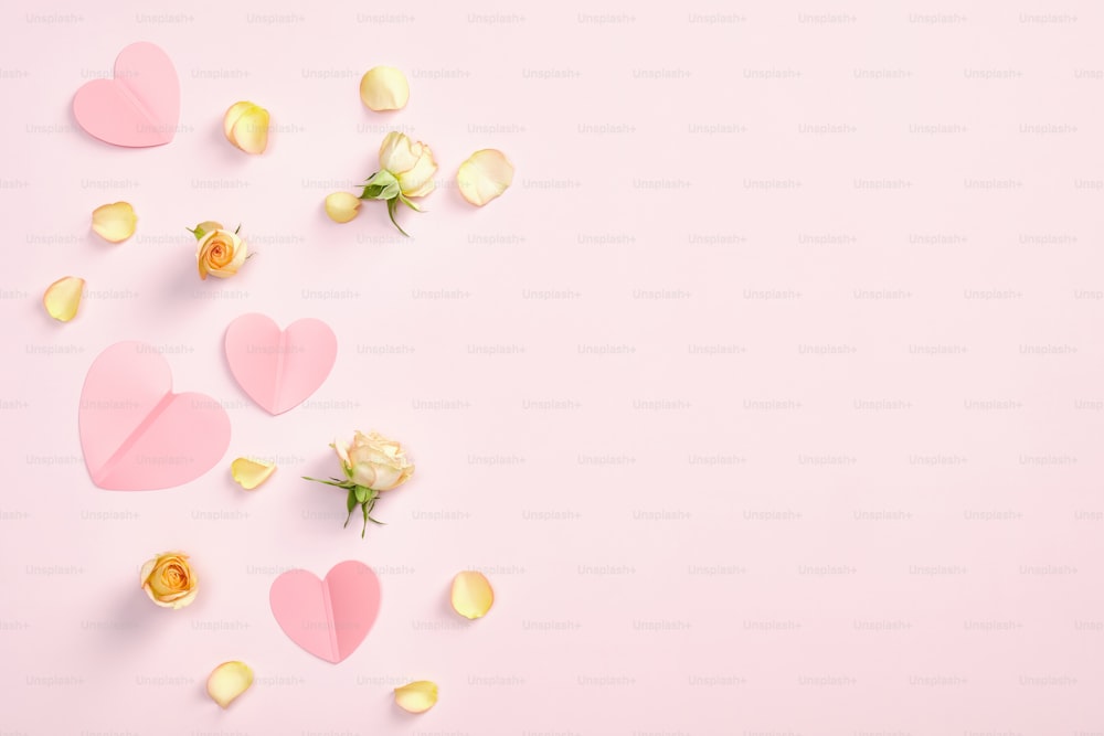 Flat lay composition with paper hearts, rose flowers and petals on pink background. Romantic, love, Valentines Day concept. Top view with copy space.