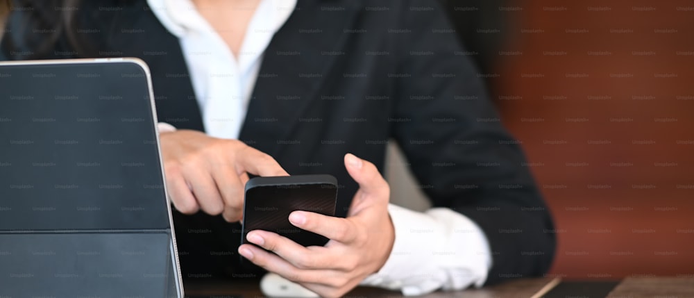 Ausschnittaufnahme einer Geschäftsfrau, die Informationen auf dem Handy sucht und im Büro mit dem Tablet arbeitet.