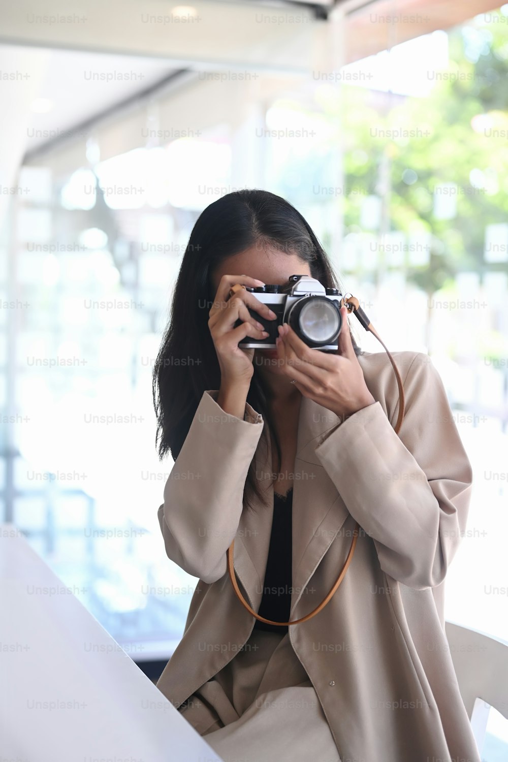Porträt einer jungen Asiatin, die an ihrem Arbeitsplatz mit einer Digitalkamera fotografiert.