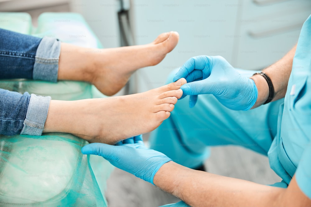 Retrato de cerca de los pies femeninos en la silla médica mientras el médico podólogo trata la uña con tecnologías médicas modernas en la clínica de belleza