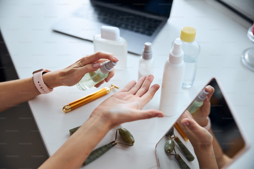 Cropped head portrait of elegant young woman hand squeezing serum on arm above the white desk in room indoors