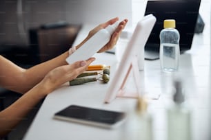 Side view portrait of woman hand with white plastic tube above the beauty desk with roller facial massager in room indoors