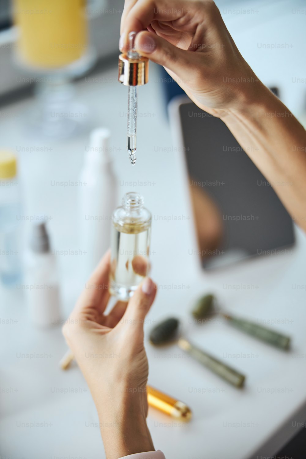 Focused image of female holding glass bottle with organic serum above the white desk in room indoors