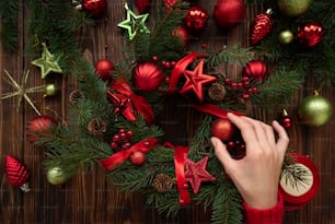 Florist hands making Christmas wreath on wooden brown background. Top view. New Year or Christmas celebration concept