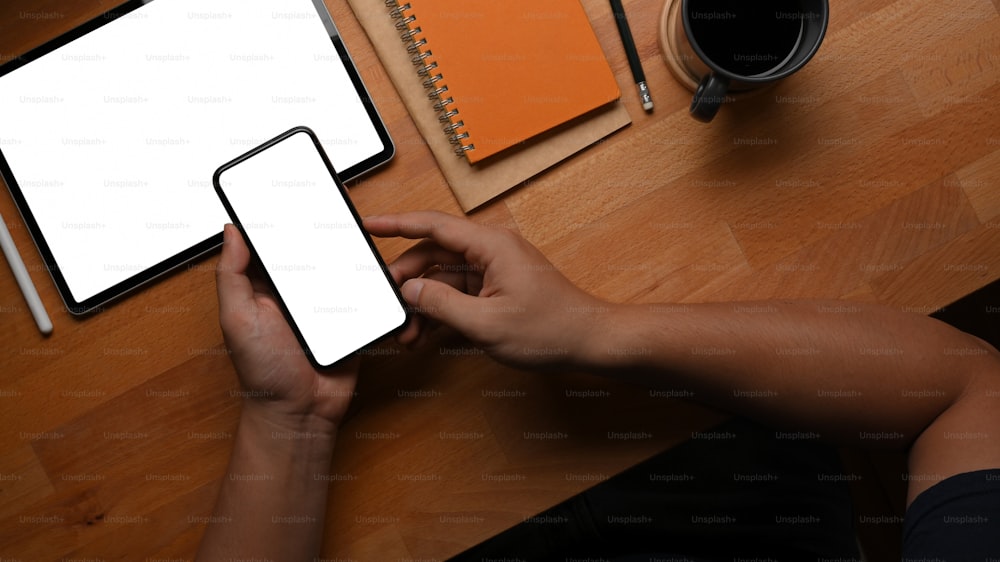 Top view of male hand using smartphone on worktable with tablet and stationery, clipping path
