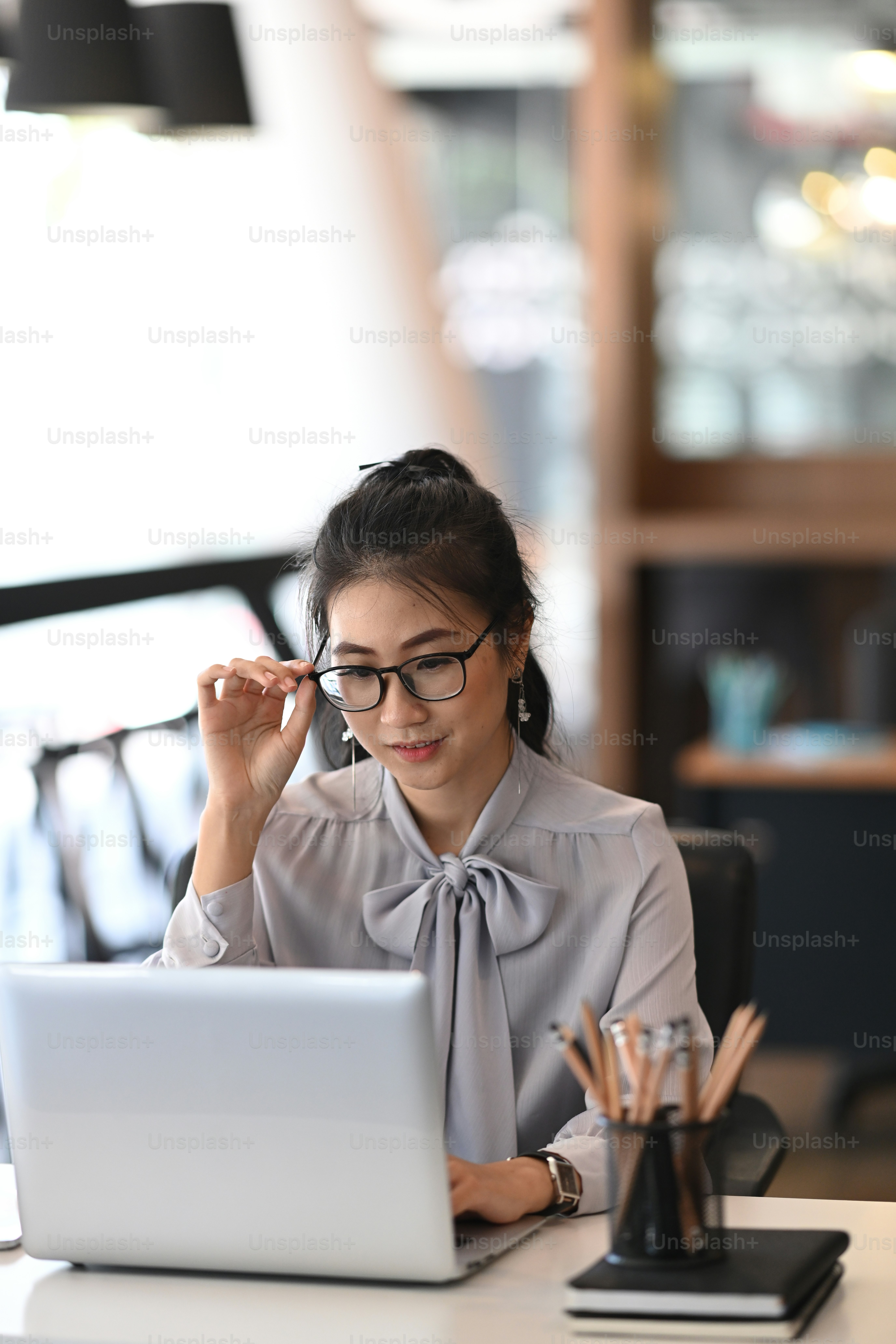 Porträt einer positiven Geschäftsfrau, die an ihrem Arbeitsplatz sitzt und ihre Brille berührt.