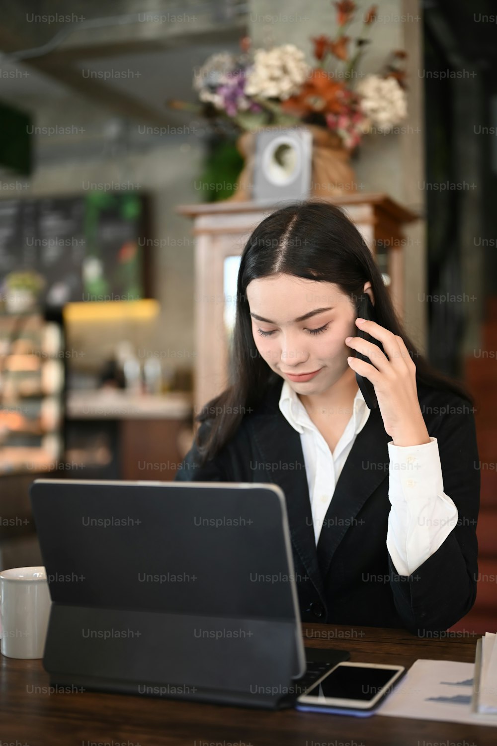 Retrato da empresária no terno preto falando no telefone celular e trabalhando no escritório moderno.