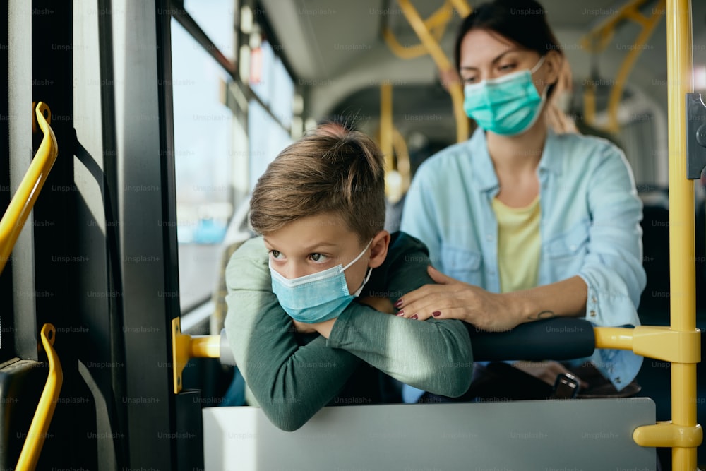 Niño pensativo y su madre con máscaras faciales protectoras mientras viajan en transporte público.