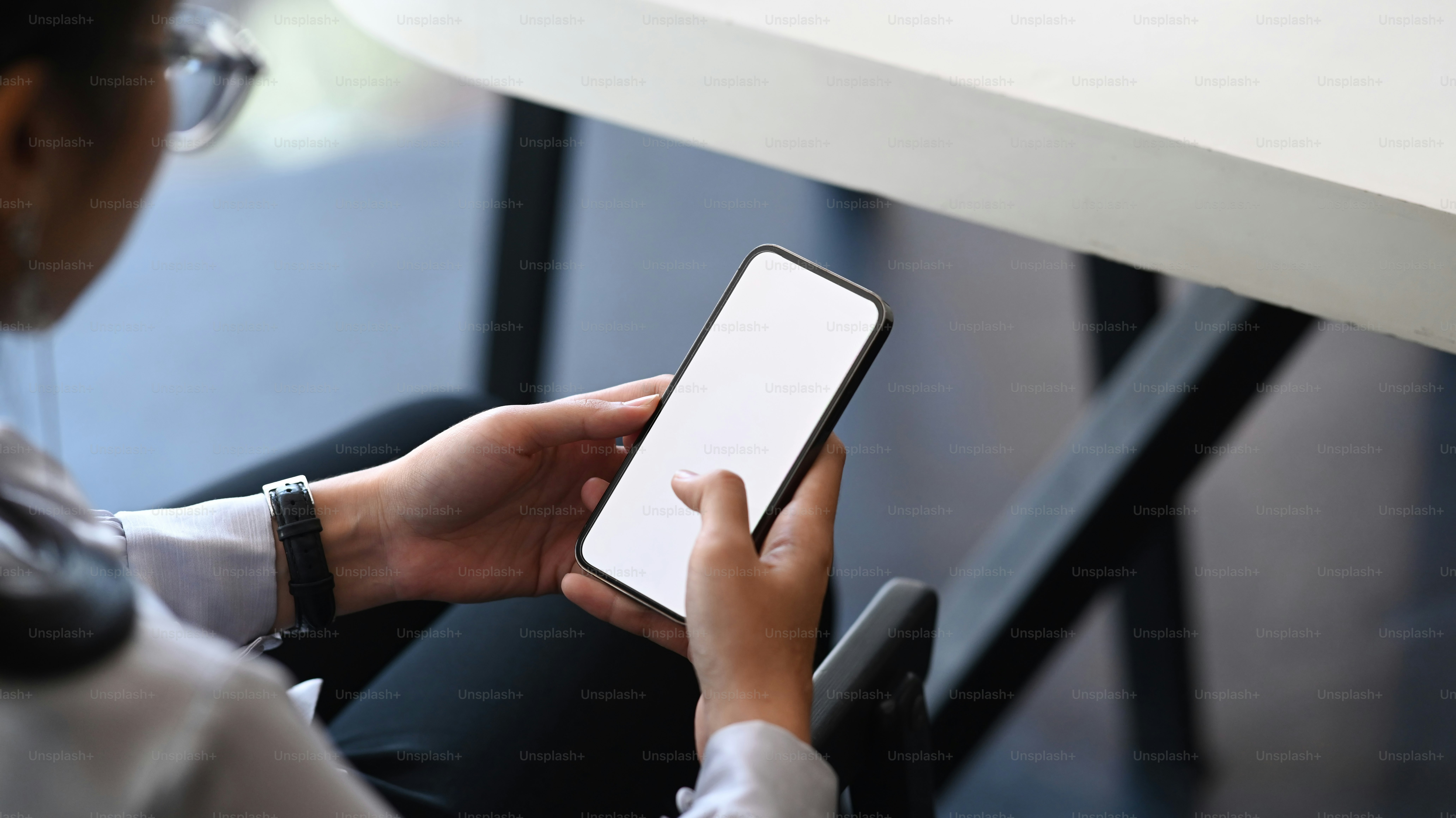 オフィスに座ってスマートフォンを使用している眼鏡の若い女性の接写。