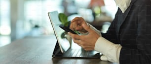 Vista lateral de las manos femeninas usando el teléfono inteligente mientras trabaja con la tableta en la mesa de la cafetería