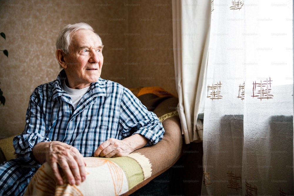 Cute grandfather sitting at the armchair in a living room and looking to the window. Happy oldness concept