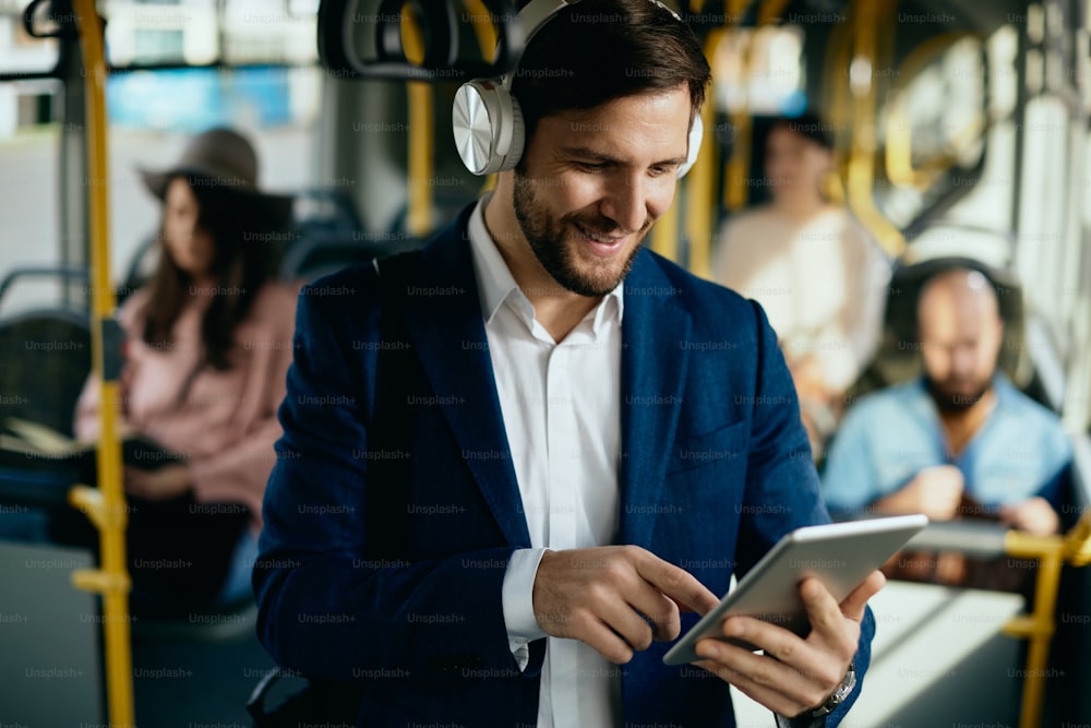 헤드폰을 착용하고 버스로 출퇴근하는 동안 디지털 태블릿을 사용하는 행복한 사업가.