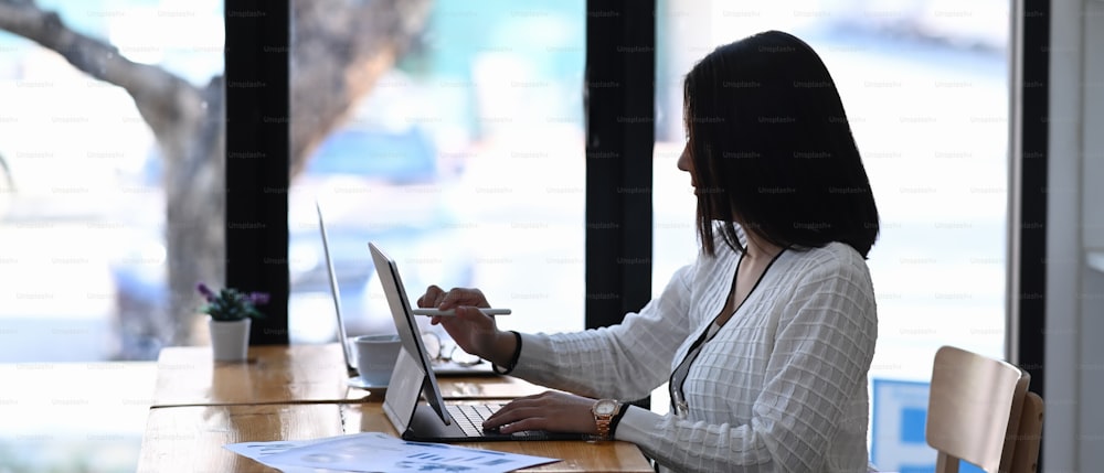 Vista laterale della donna d'affari che lavora su tablet computer alla scrivania di lavoro in un ufficio moderno.