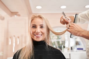 Reinicie sua vida. Mulher loira jovem cortando o cabelo em cabeleireiros. Close up do cabeleireiro cortando o cabelo para um nível reto. Cabeleireiro usando pente e tesoura para um corte de cabelo