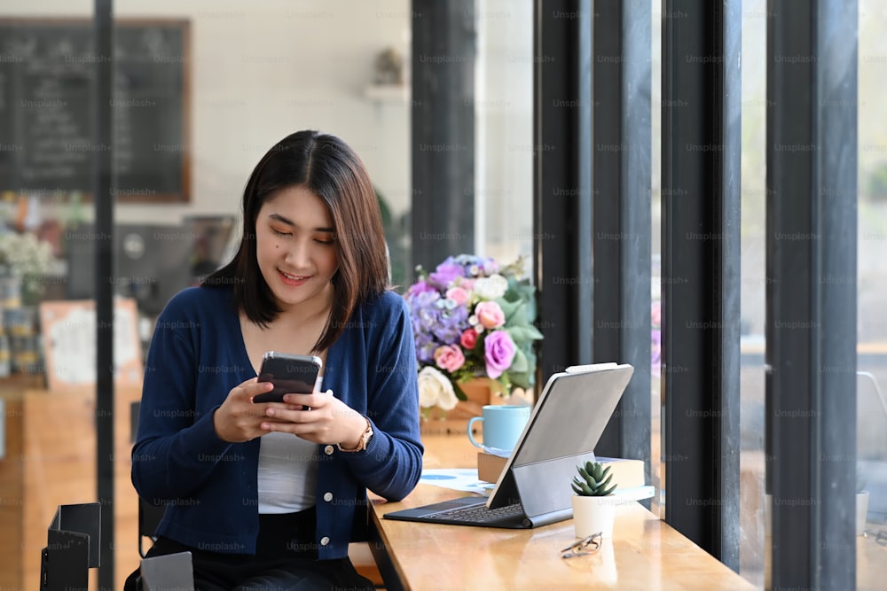 Mulher alegre conversando on-line nas redes sociais com amigo no smartphone enquanto está sentada no escritório.