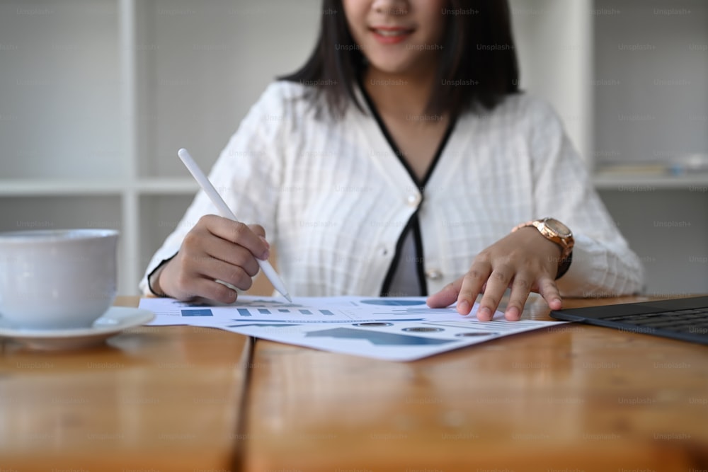 Close up view of businesswoman hand holding pen and pointing at financial paperwork.