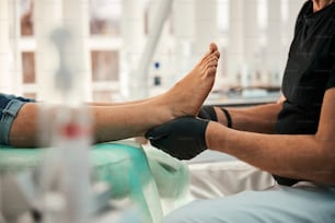 Professioneller Podologe sitzt in halber Position, während er medizinische Behandlungen für Patienten durchführt