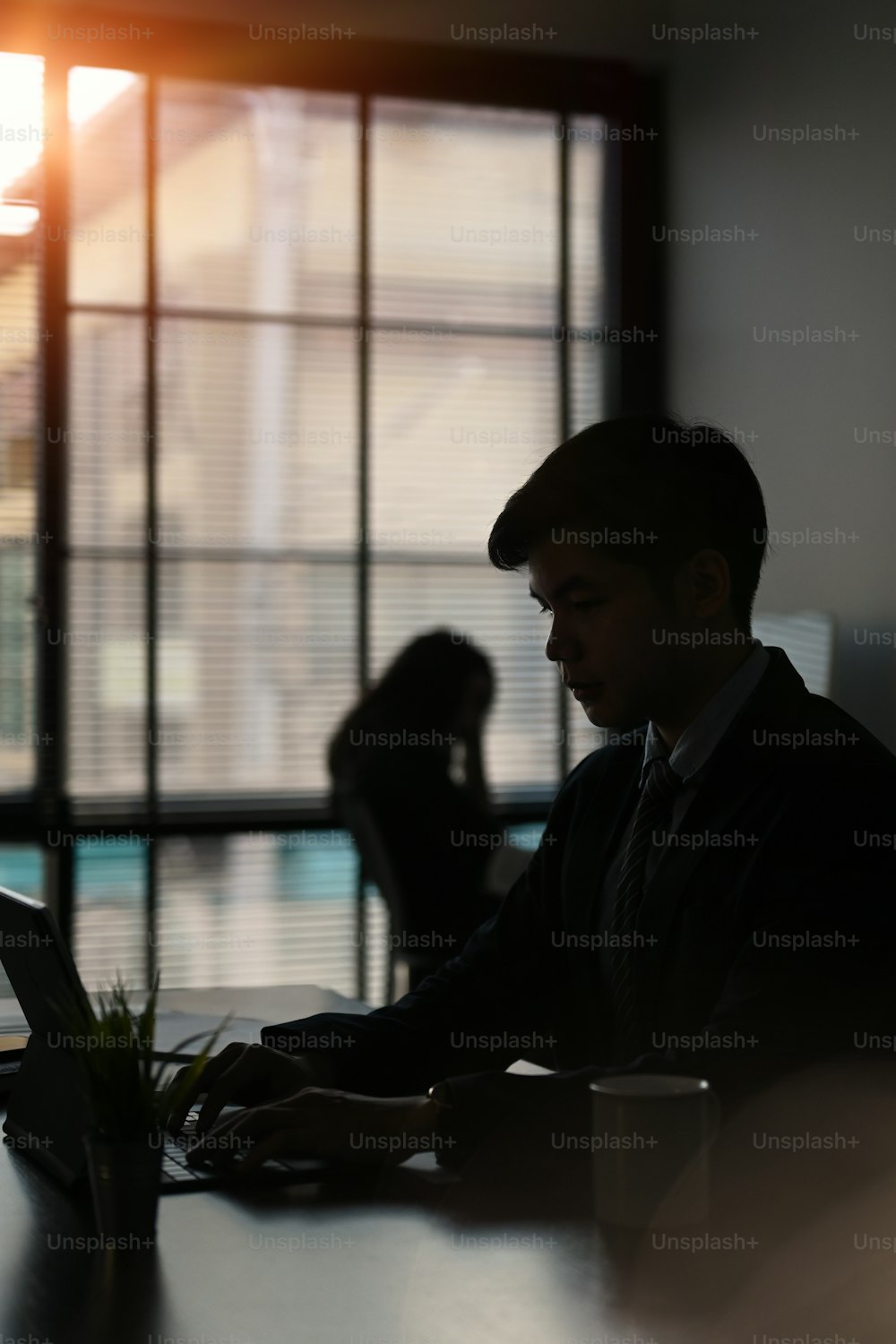 Silhouettes of businessman working with computer tablet and sitting with his colleagues in modern office.