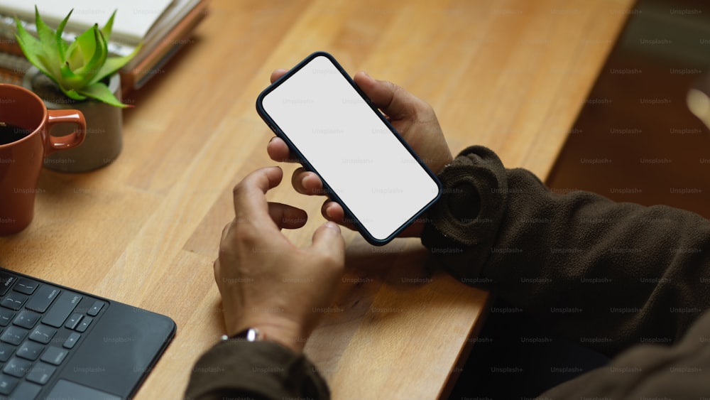 Beschnittene Aufnahme von männlichen Händen mit Smartphone auf Holztisch, einschließlich Clipping-Pfad