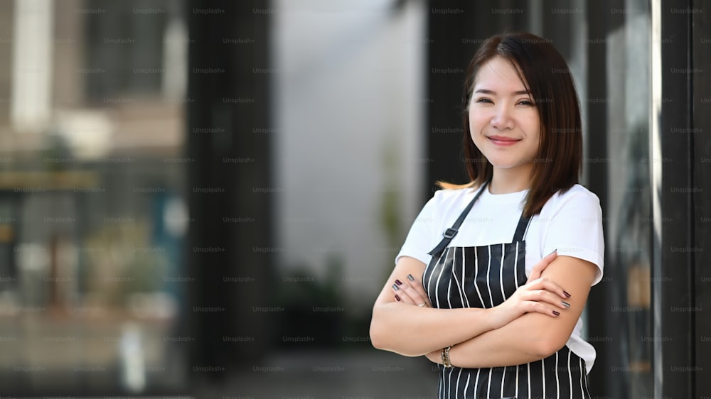 Cheerful smiling female in black apron standing with arms crossed and smiling to camera.
