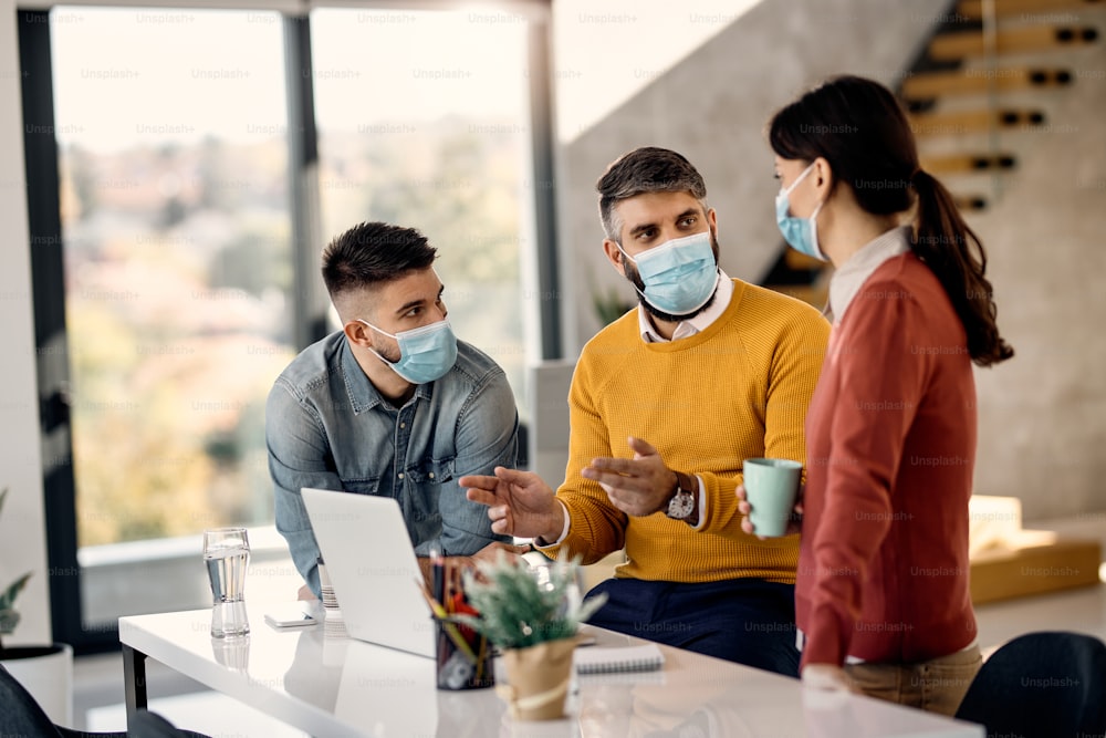 Mid adult manager using computer and talking to his team while working in the office during coronavirus pandemic.