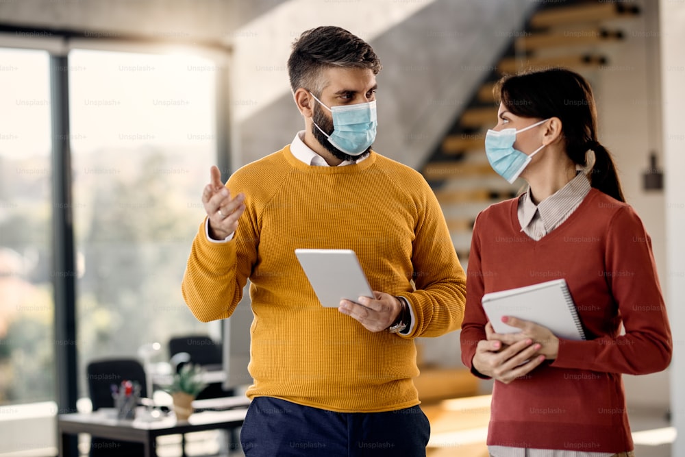 Business coworkers talking while wearing face masks and working in the office.