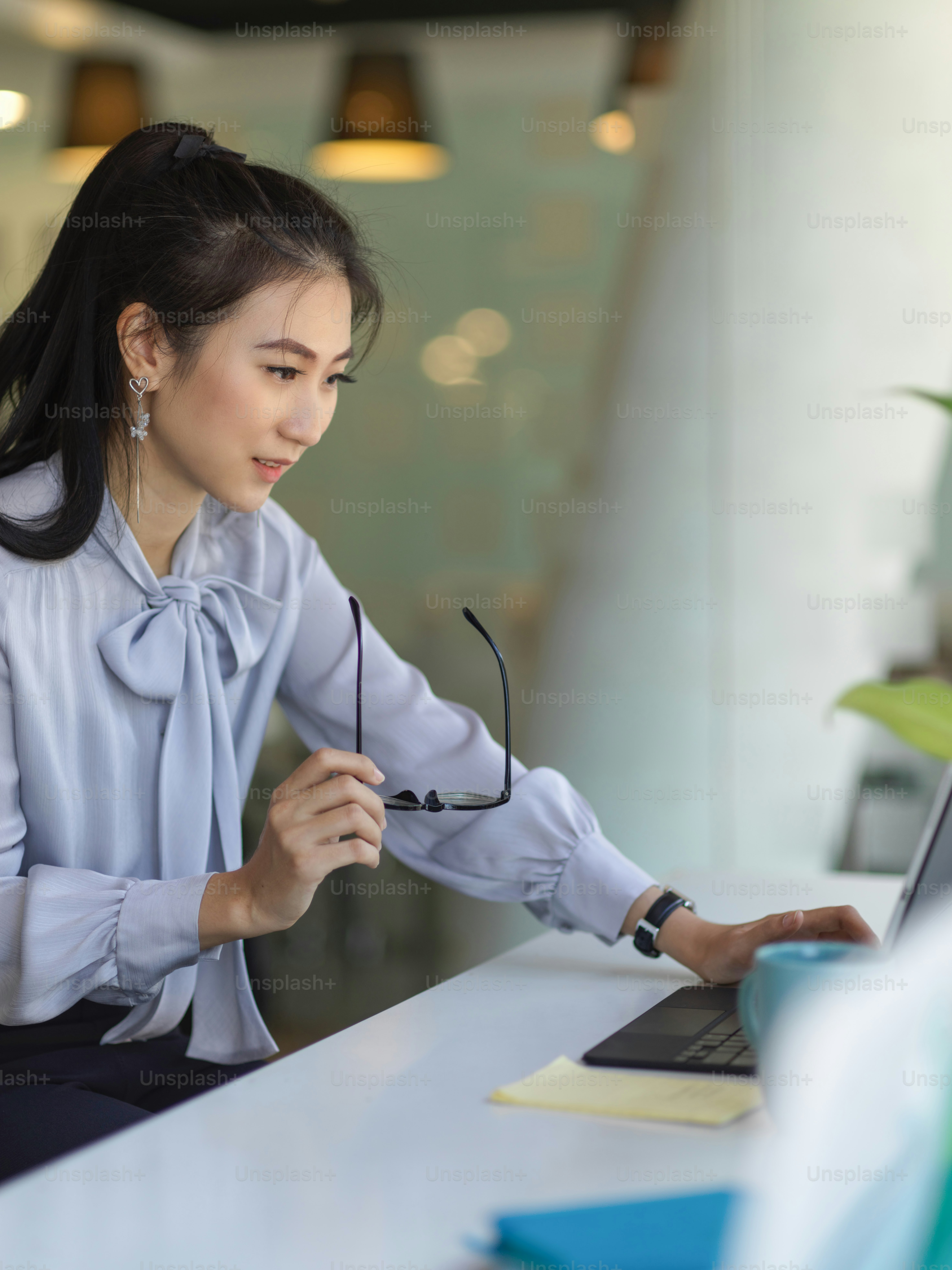 Side view of young female office worker working with office supplies and holding eyeglasses