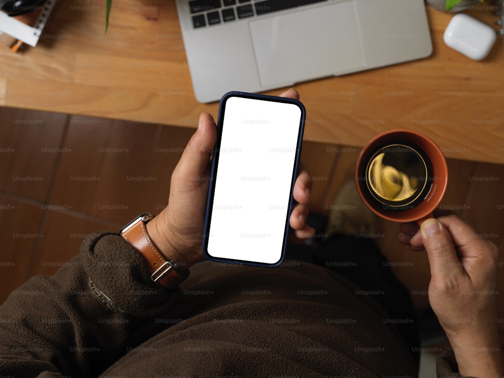 Top view of male hand holding smartphone and coffee cup above worktable