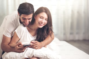 couple using mobile phone on white bed in morning time