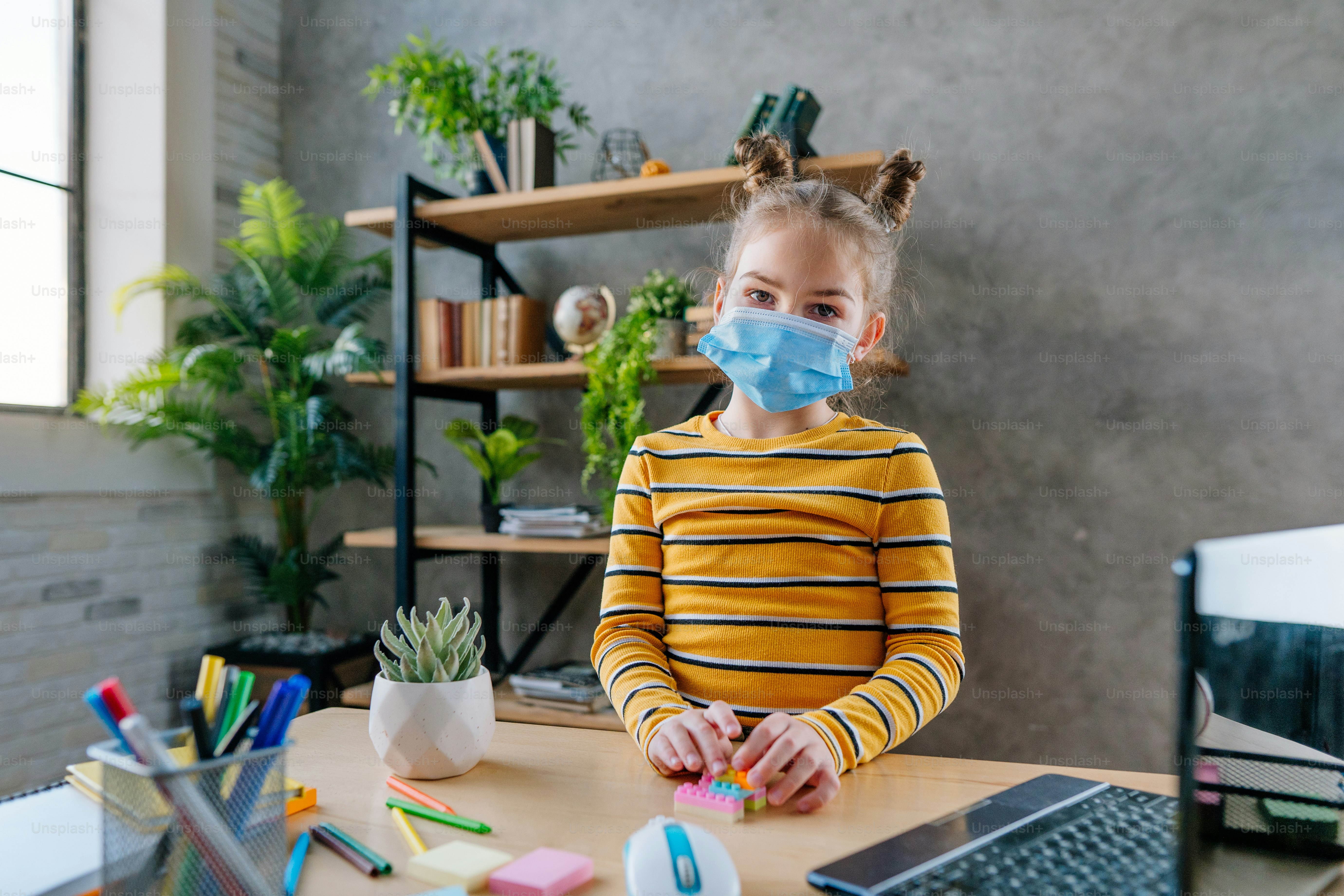 Fille de 8 ans dans le masque facial jetable médical étudiant en ligne à la maison à l’aide d’un ordinateur portable dans la chambre. Concept d’enseignement à distance pendant le confinement lié à la pandémie.