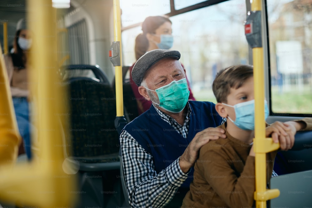 행복한 노인과 그의 손자는 코로나 바이러스 전염병으로 인해 대중 버스로 여행하고 보호용 안면 마스크를 착용합니다.