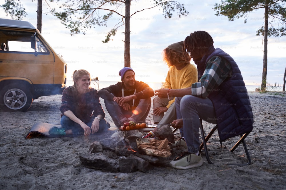 Happy friends at a picnic is preparing a barbecue grill outdoors. Cheerful people sitting at the circle and chatting before the dinner