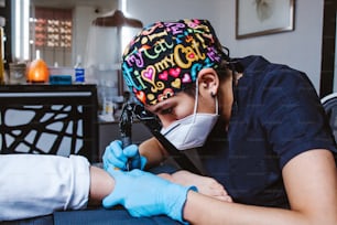 Latin woman tattoo artist demonstrates the process of getting tattoo with paint and works in blue sterile gloves in Mexico city