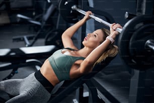 Athlete tensing her hands muscles while lifting a weight over her head on a gym press bench