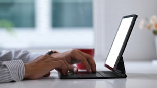 Vista de perto das mãos do empresário digitando no teclado do tablet em seu espaço de trabalho.